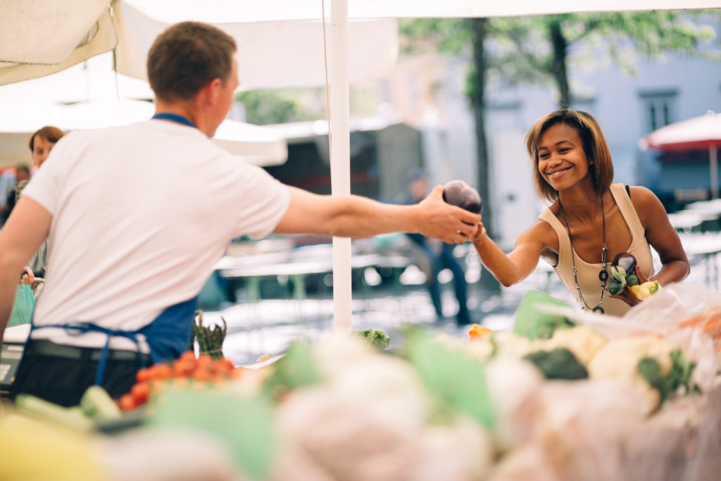 A seller passing produce to a customer at a farm market